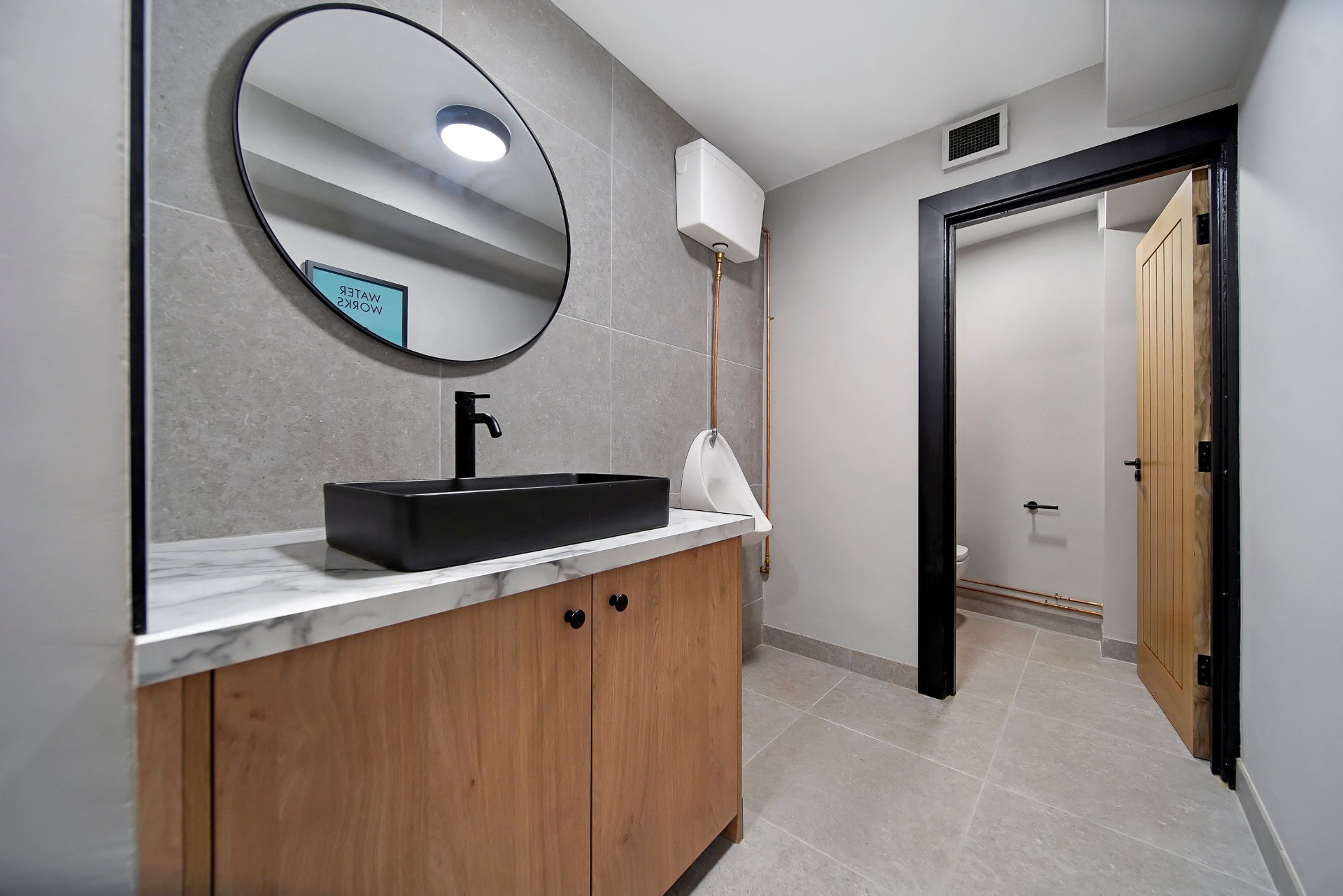 Gents washroom at Patrick's with black basin, round mirror and separate cubicle