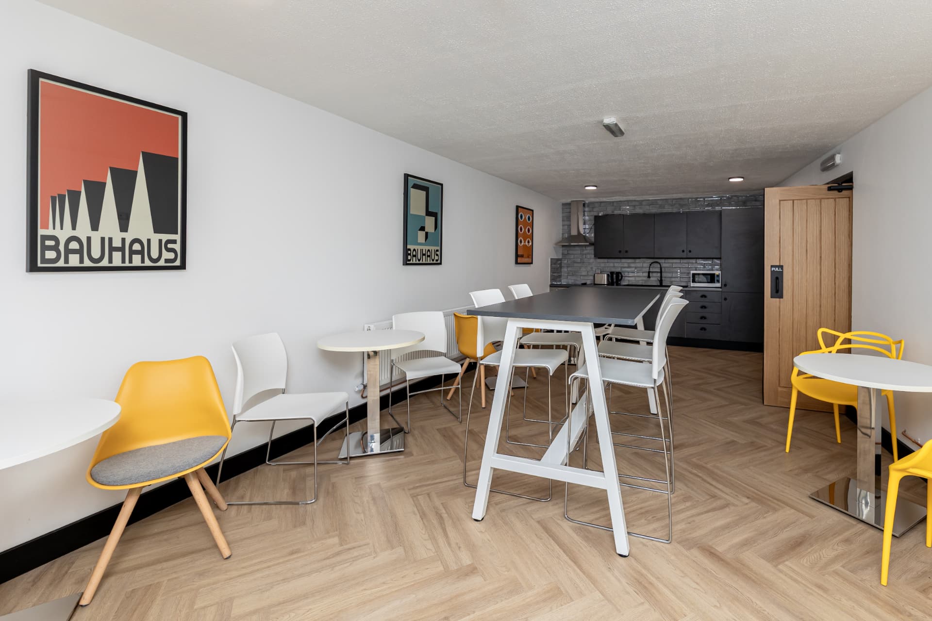 Bright kitchen and breakout area at Patrick's with Bauhaus prints, high tables, and yellow chairs