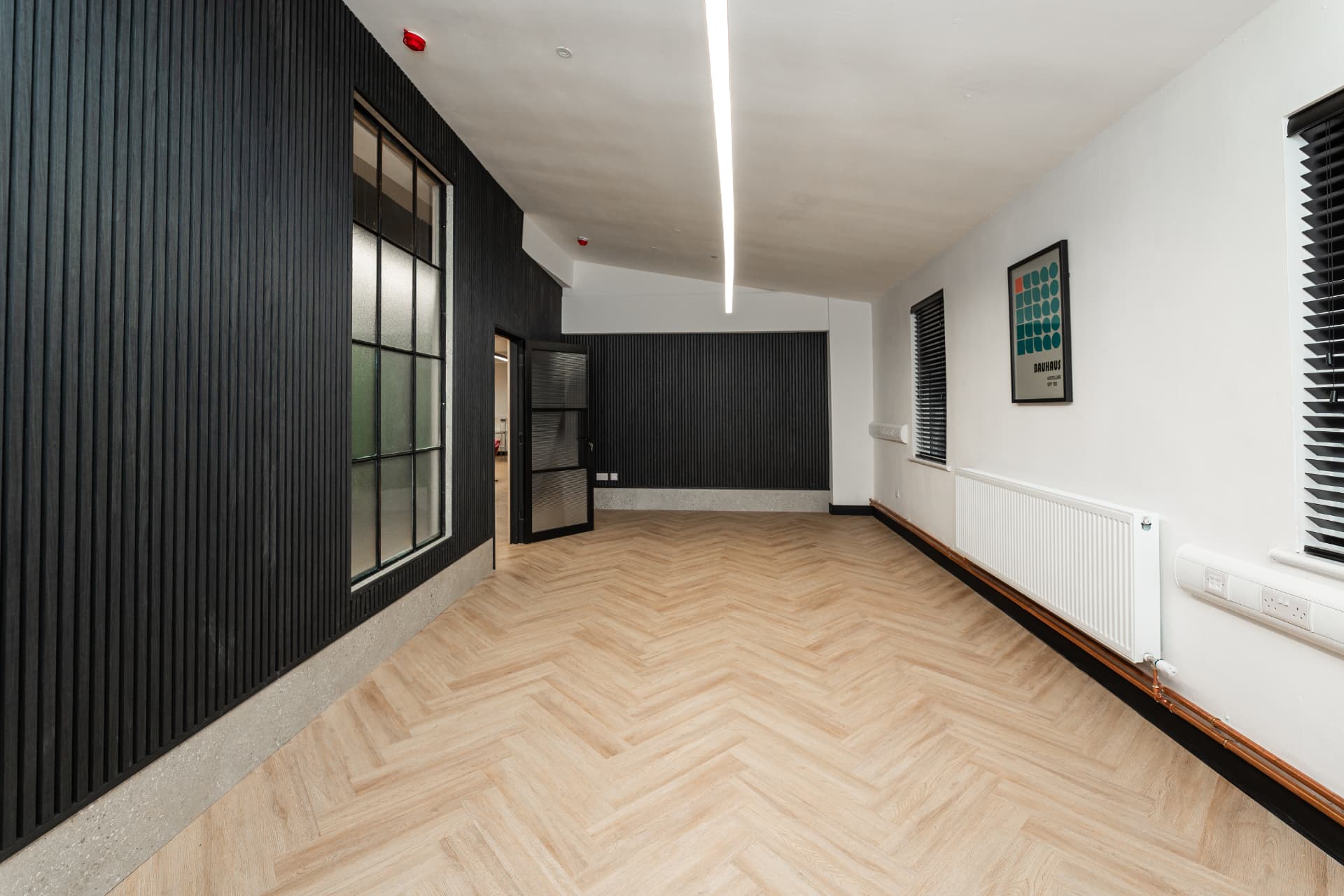 Large private room at Workpoint with black slatted walls, herringbone flooring and feature lighting